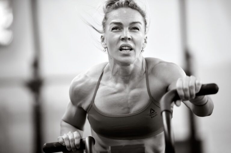 A focused woman in a sports bra intensely working out on exercise equipment, showcasing fitness and determination.